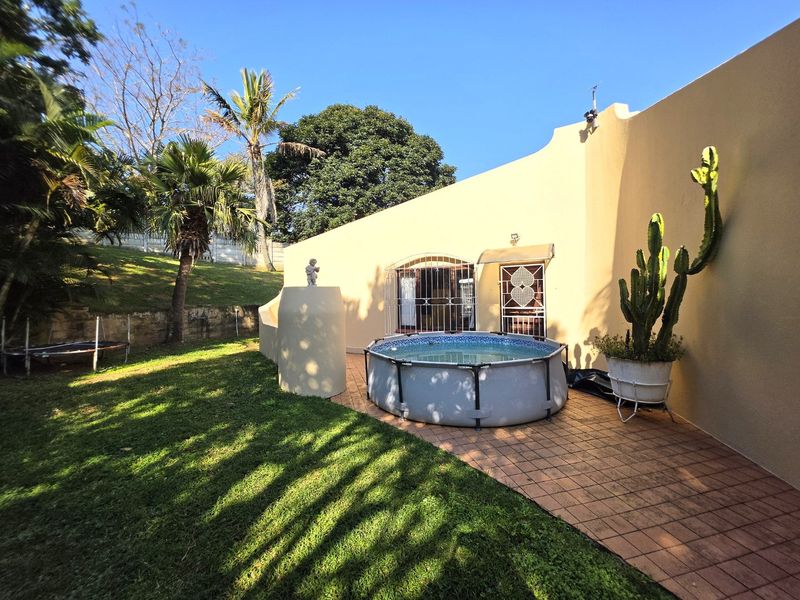 Rear exterior view featuring a tiled patio area, landscaped garden, and security-gated access to the main dwelling.