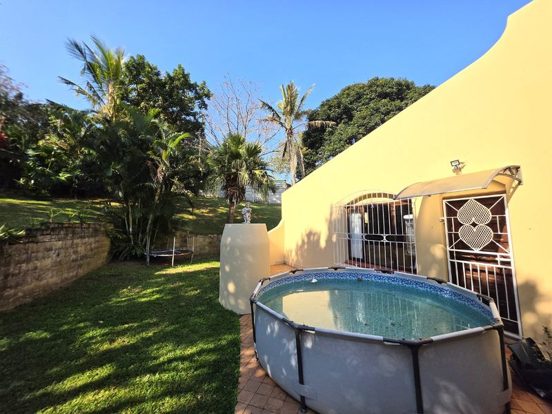 Outdoor area featuring an above-ground pool, paved patio space, and a landscaped garden with a retaining wall.