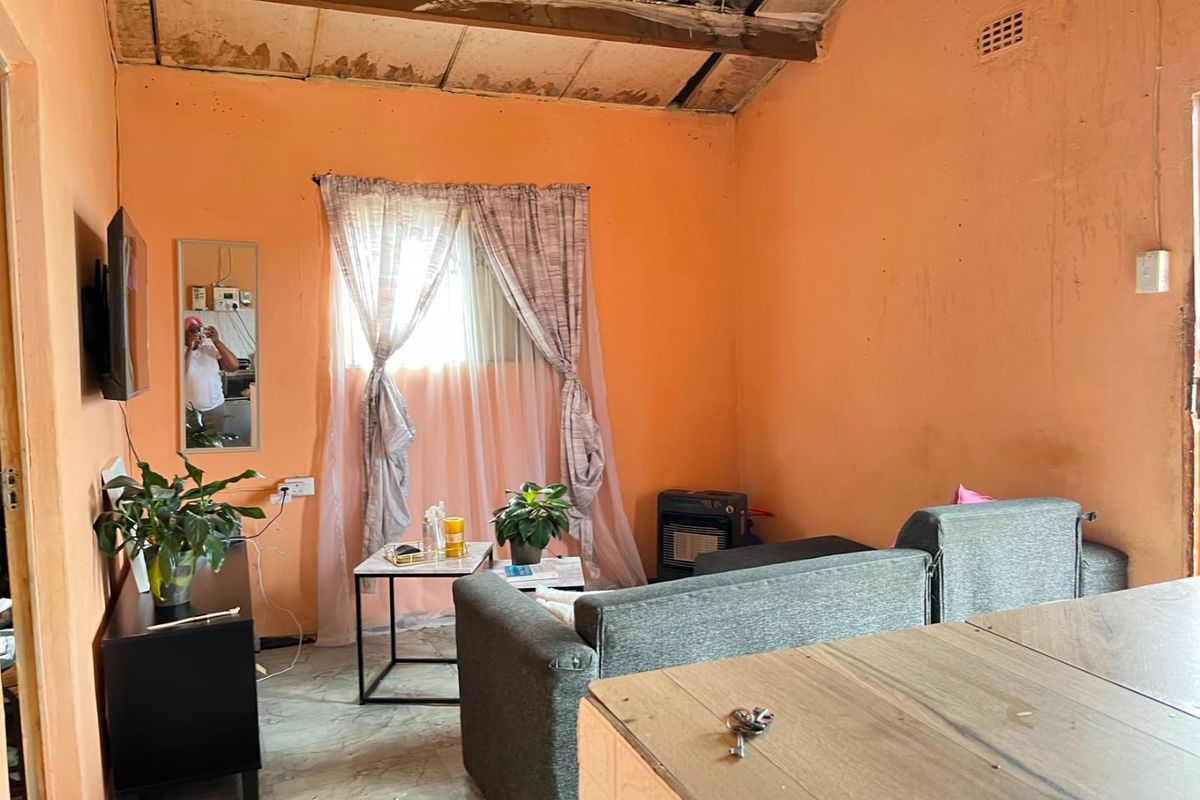 A living room featuring exposed ceiling beams and a dated interior finish, requiring cosmetic updates to improve the overall aesthetic and condition.