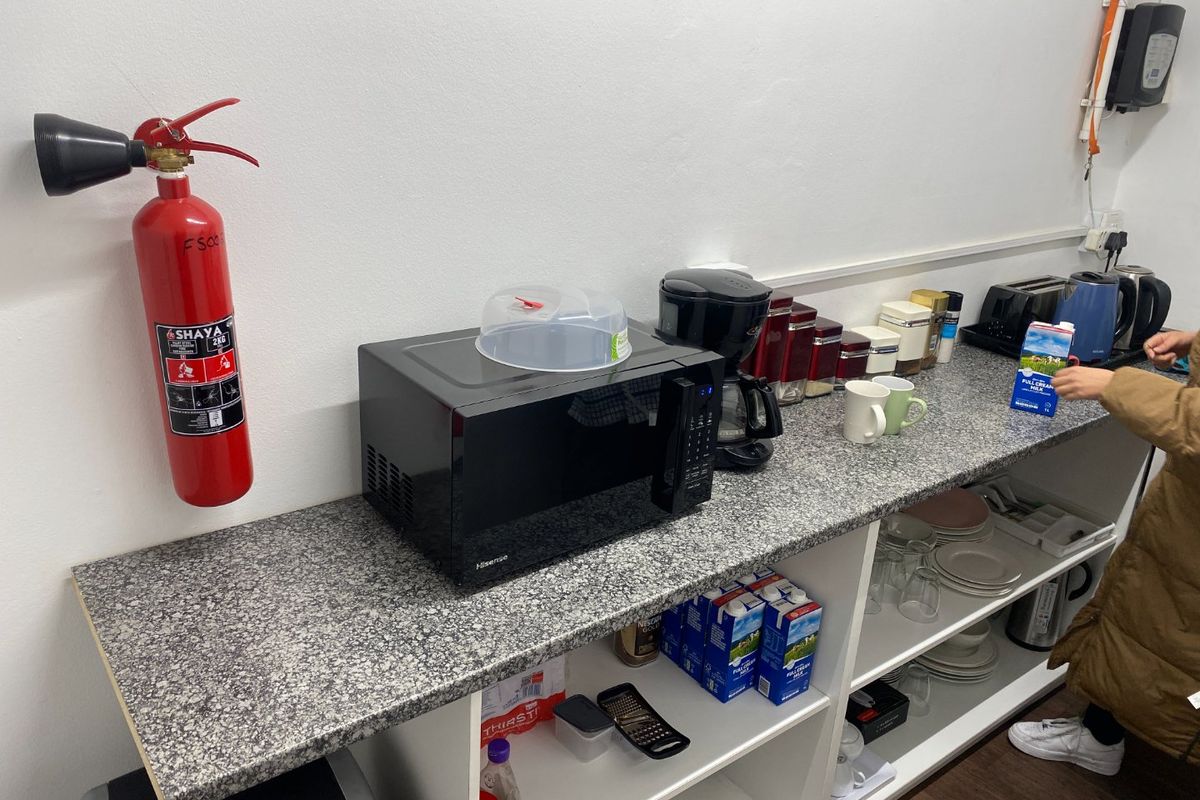A functional kitchenette area featuring a granite countertop, open storage shelving, and a wall-mounted fire extinguisher for safety.