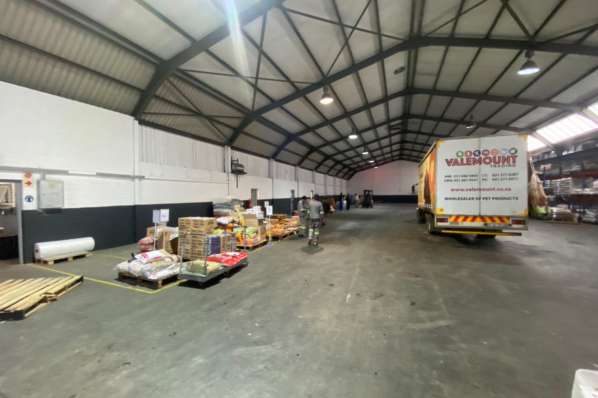 Spacious industrial warehouse featuring high exposed steel truss ceilings, durable concrete flooring, and functional overhead lighting, suitable for logistics or storage operations.