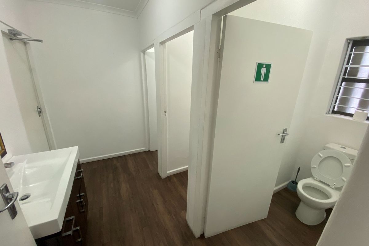 A clean, functional industrial bathroom facility featuring a vanity basin, toilet, and durable laminate flooring with secure window bars.