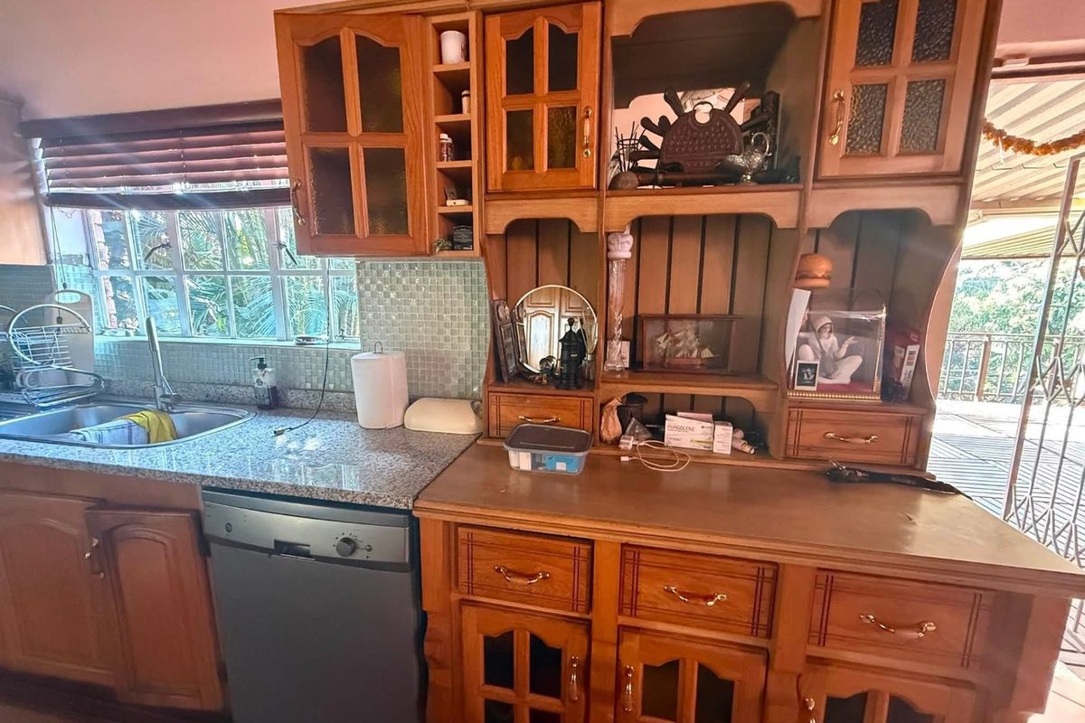 A kitchen featuring traditional wooden cabinetry, granite countertops, a mosaic tile backsplash, and an integrated dishwasher with views to the outdoor patio area.