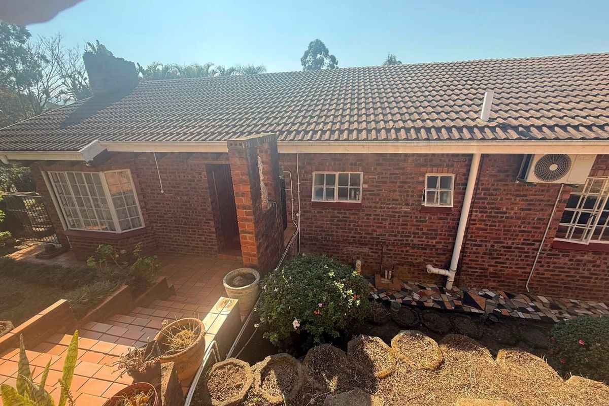 Rear exterior view of a brick-faced house featuring a tiled roof, patio area, and installed air conditioning unit.