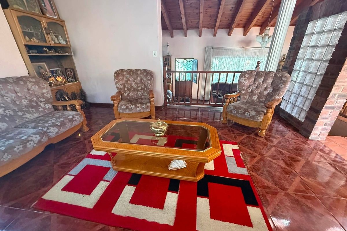 Spacious living area featuring exposed timber ceiling beams, decorative glass block wall, and tiled flooring with a classic open-plan layout.