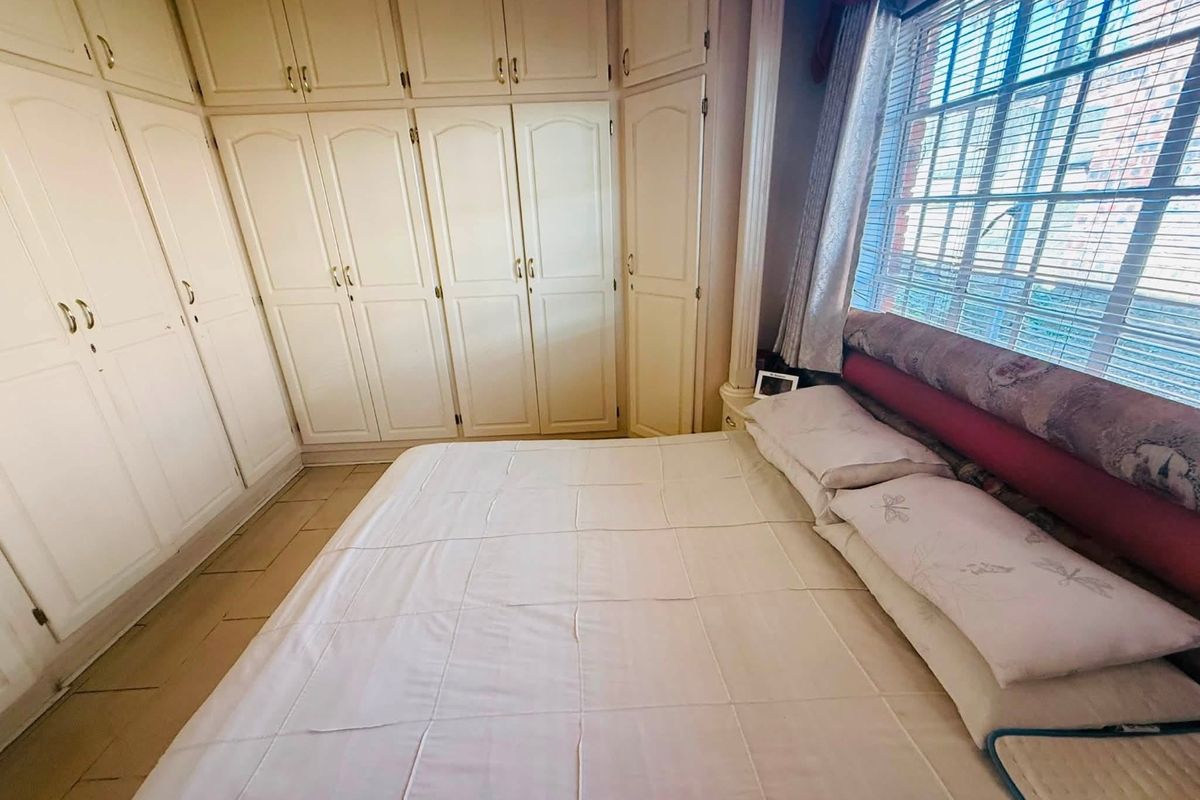 A bedroom featuring extensive built-in cabinetry, tiled flooring, and natural light through a window with fitted blinds.