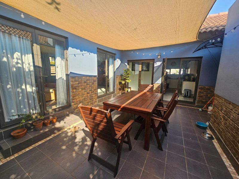 A covered outdoor patio area featuring tiled flooring, brick accents, and shade sail, providing seamless access to the interior living spaces.