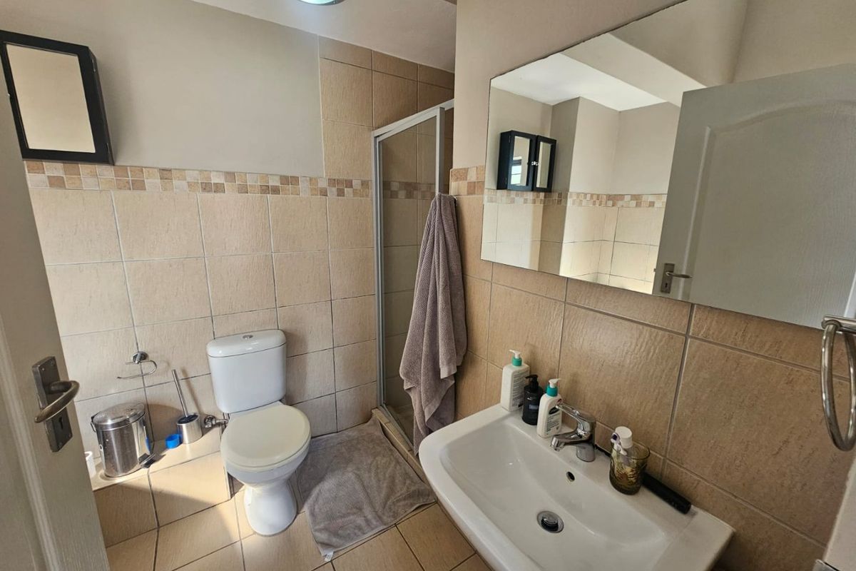 A functional bathroom featuring a shower enclosure, pedestal basin, and toilet with neutral wall and floor tiling.