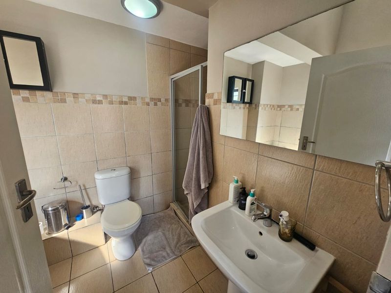 A functional bathroom featuring a shower enclosure, pedestal basin, and toilet with neutral wall and floor tiling.