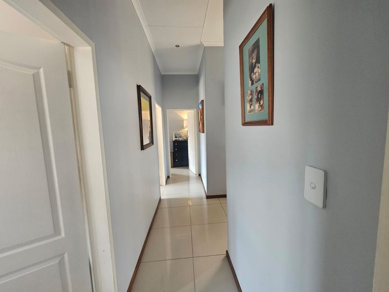 A clean and well-maintained hallway featuring neutral wall tones, tiled flooring, and recessed downlighting, providing access to adjacent rooms.