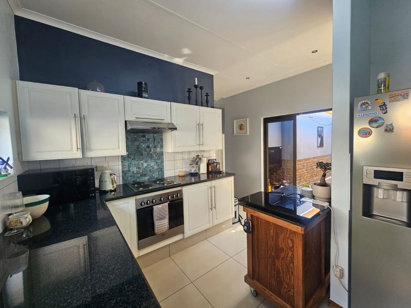 A functional kitchen featuring white cabinetry, dark granite countertops, a mosaic tile backsplash, and integrated cooking appliances with direct access to an outdoor area.