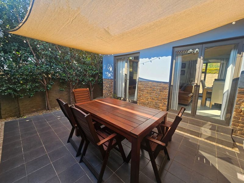 A covered outdoor patio area featuring tiled flooring, brick wall accents, and a shade sail, providing seamless access to the interior living space.