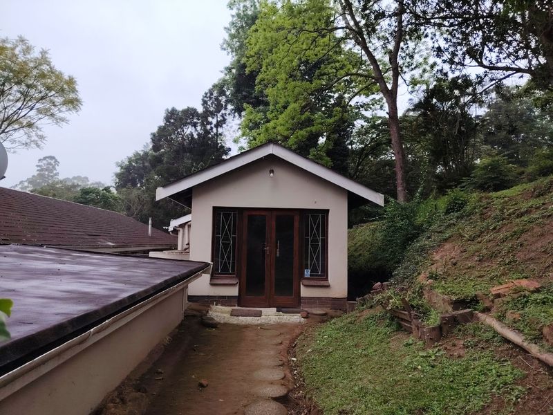 Rear view of a detached structure featuring timber-framed glass double doors and security-barred windows, set within a natural, sloped garden environment.
