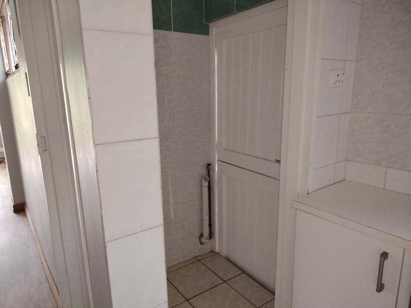 A small laundry or utility area featuring tiled walls and flooring, with a stable door and exposed plumbing connections.