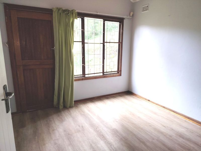 An empty bedroom featuring laminate flooring, a timber door, and a leaded glass window with natural light.