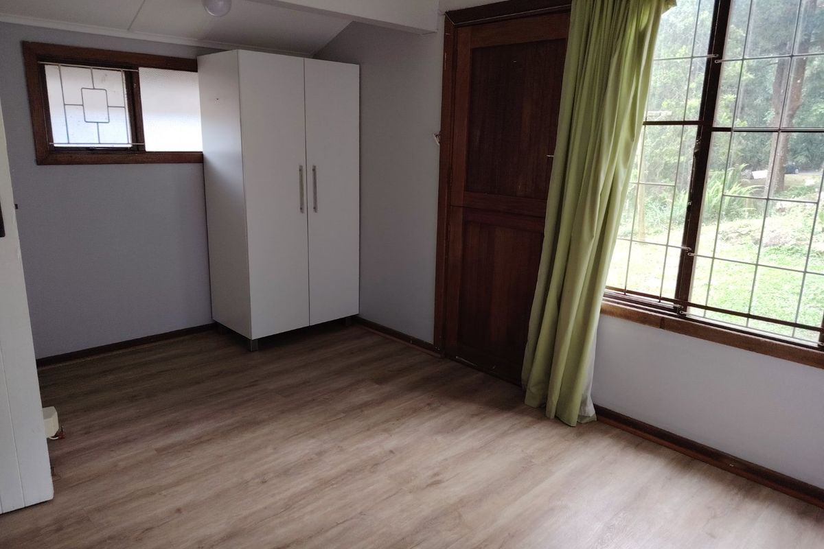 A bedroom featuring laminate flooring, timber window frames with security bars, and a timber door, offering a clean and functional space.