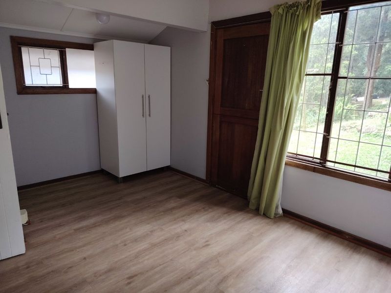 A bedroom featuring laminate flooring, timber window frames with security bars, and a timber door, offering a clean and functional space.