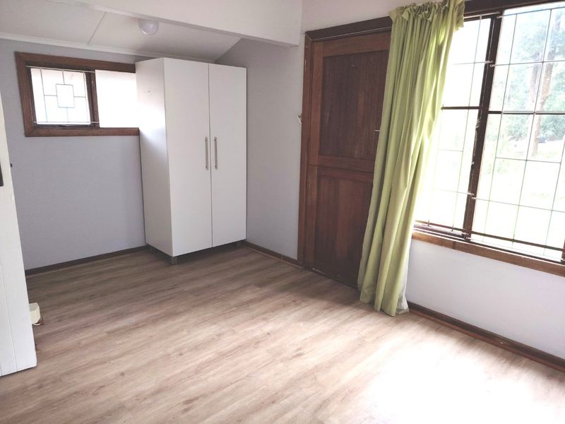 A bright, empty bedroom featuring laminate flooring, timber-framed windows, and a solid timber door, offering a neutral canvas for personalization.