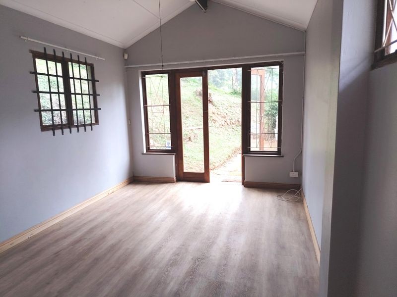 A bright, empty living room featuring vaulted ceilings, light-toned laminate flooring, and direct access to the outdoors through a timber-framed glass door.