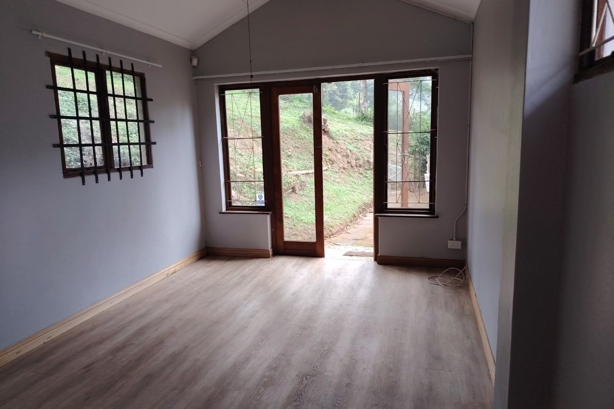 An empty living room featuring vaulted ceilings, timber-look laminate flooring, and direct access to the outdoor area through a timber-framed glass door.