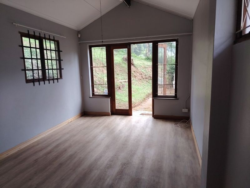 An empty living room featuring vaulted ceilings, timber-look laminate flooring, and direct access to the outdoor area through a timber-framed glass door.