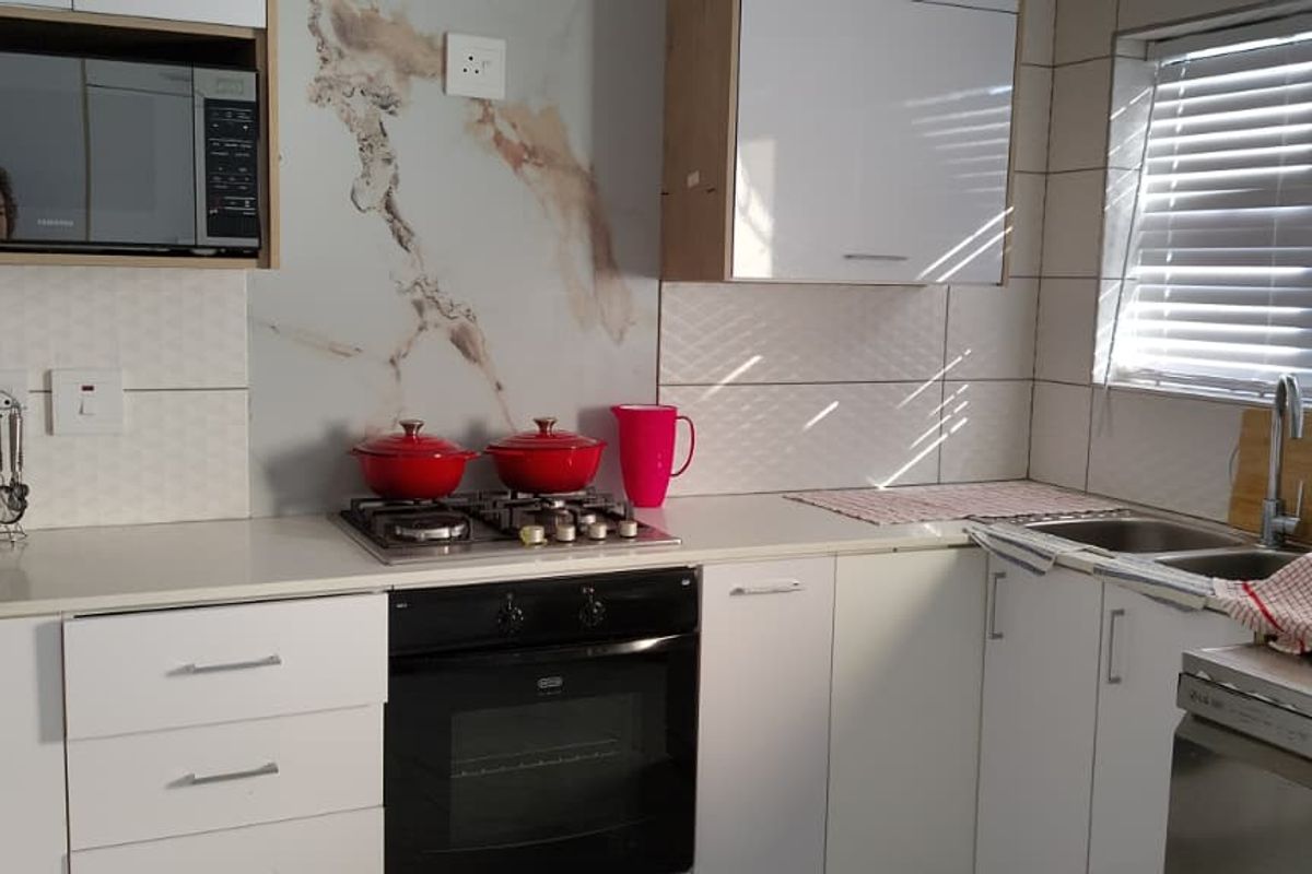Modern kitchen featuring white cabinetry, stone countertops, a marble-look splashback, built-in oven, gas hob, and a double sink with a mixer tap.