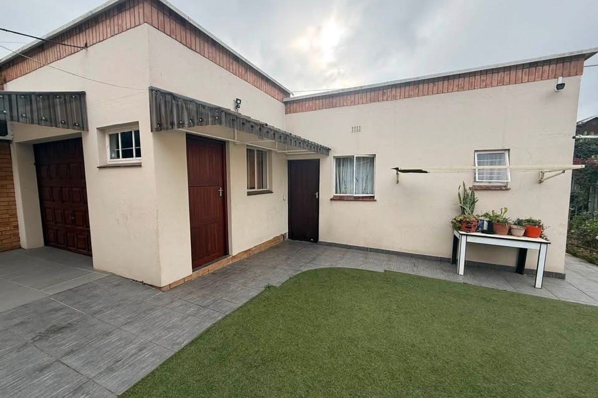 Rear exterior view of the house featuring a tiled patio area, artificial lawn, and direct access to the garage and main dwelling.