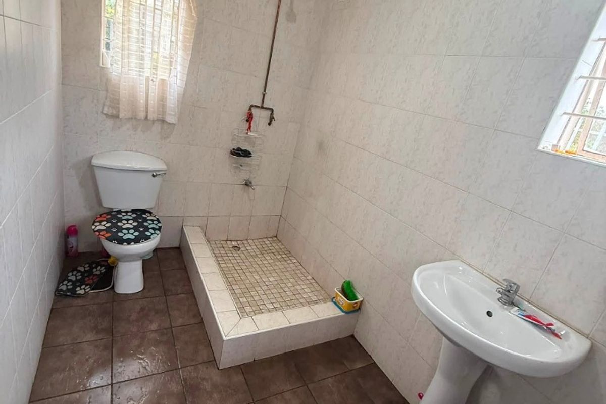 A functional bathroom featuring a pedestal basin, toilet, and a tiled shower cubicle. The space shows signs of wear and requires cosmetic updates.