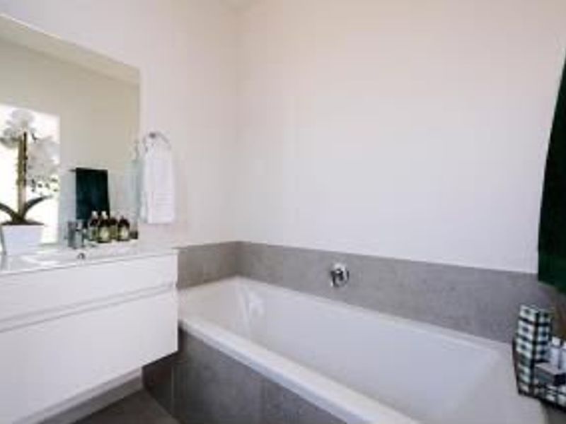Modern bathroom featuring a wall-mounted vanity with integrated basin, large mirror, and a built-in bathtub with neutral tiled surround.
