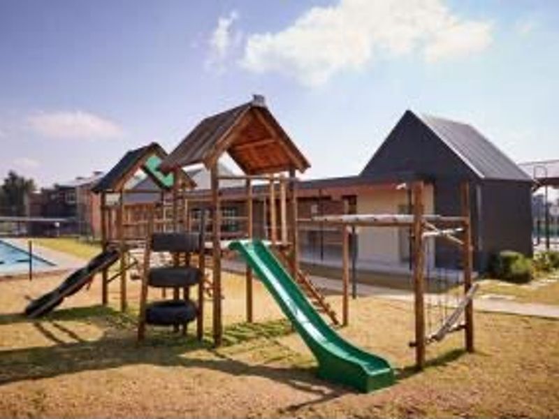 Communal outdoor area featuring a playground with wooden structures and a swimming pool set within a landscaped residential complex.