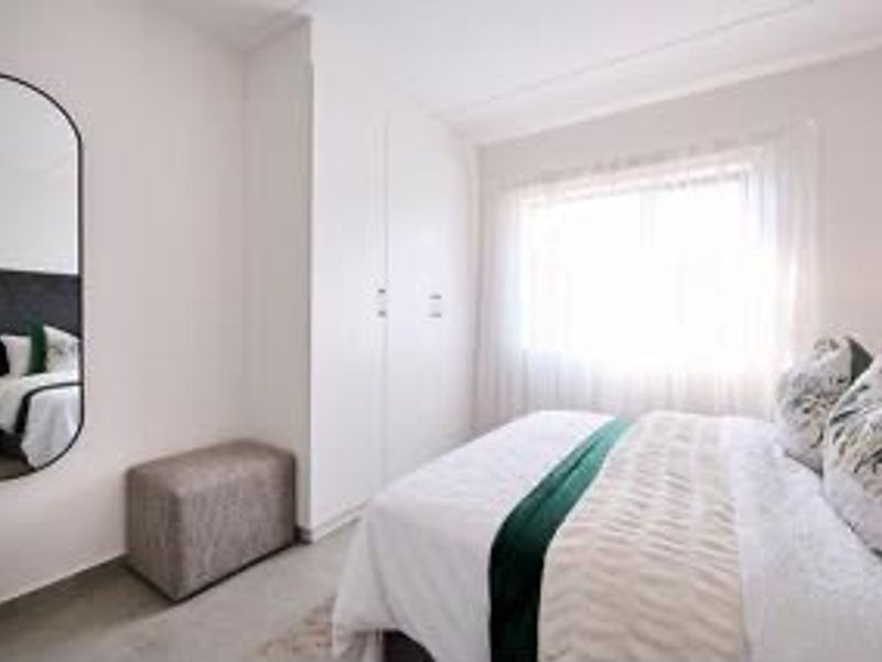 A bright and well-maintained bedroom featuring built-in wardrobes and a large window, offering a clean and neutral living space.