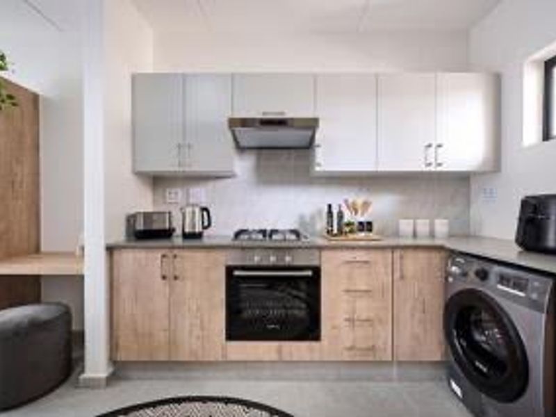 Modern kitchen featuring light wood-look cabinetry, stone countertops, built-in oven and hob, extractor fan, and integrated space for laundry appliances.