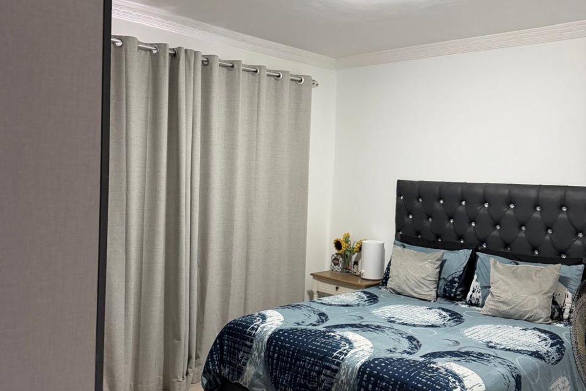 A well-maintained bedroom featuring neutral tiled flooring, decorative ceiling cornicing, and a central light fixture.