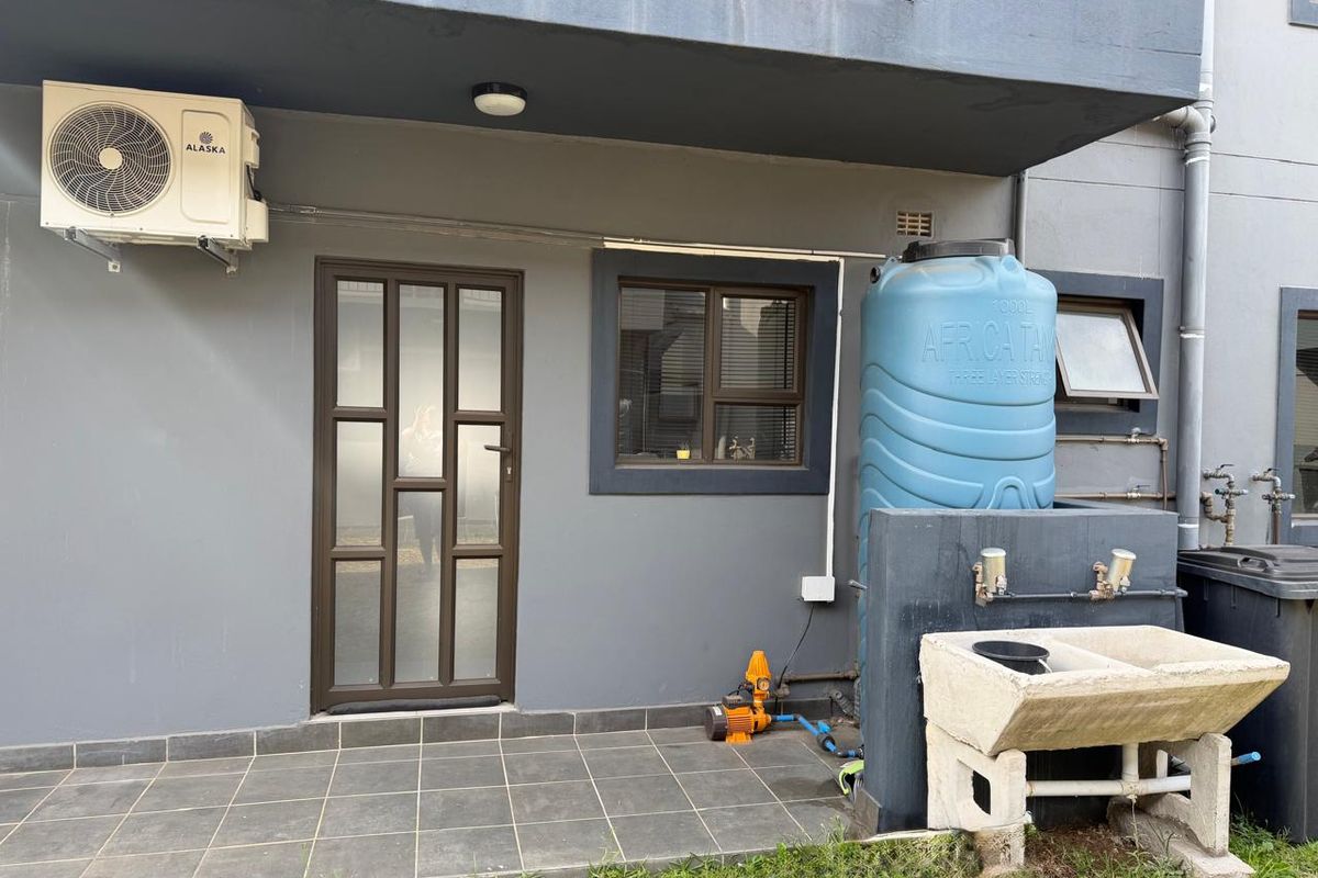 Rear exterior area featuring a tiled patio, water storage tank with pump, and a concrete laundry sink.