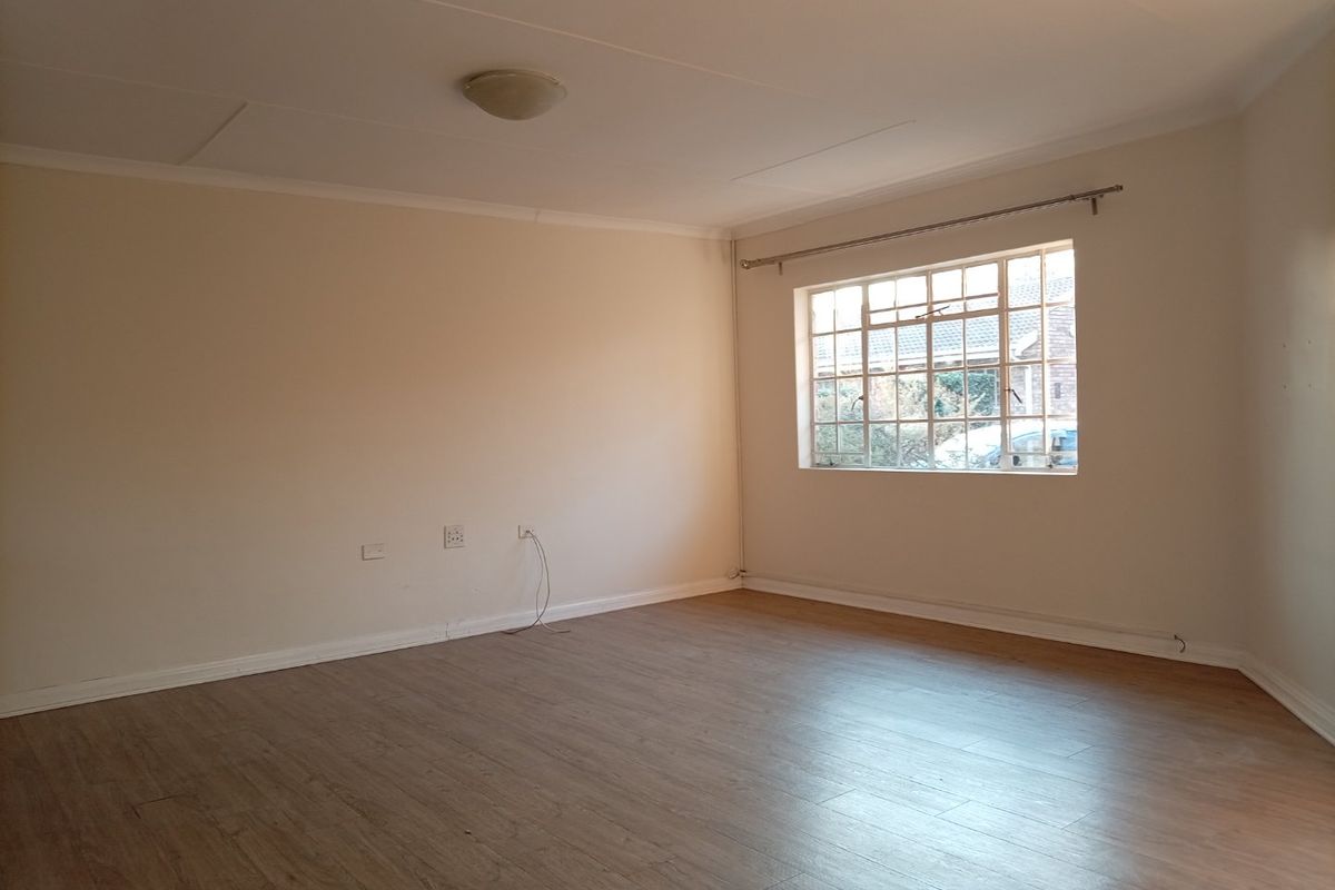 A bright, empty living room featuring neutral walls, laminate flooring, and a large steel-framed window, providing a blank canvas for interior design.