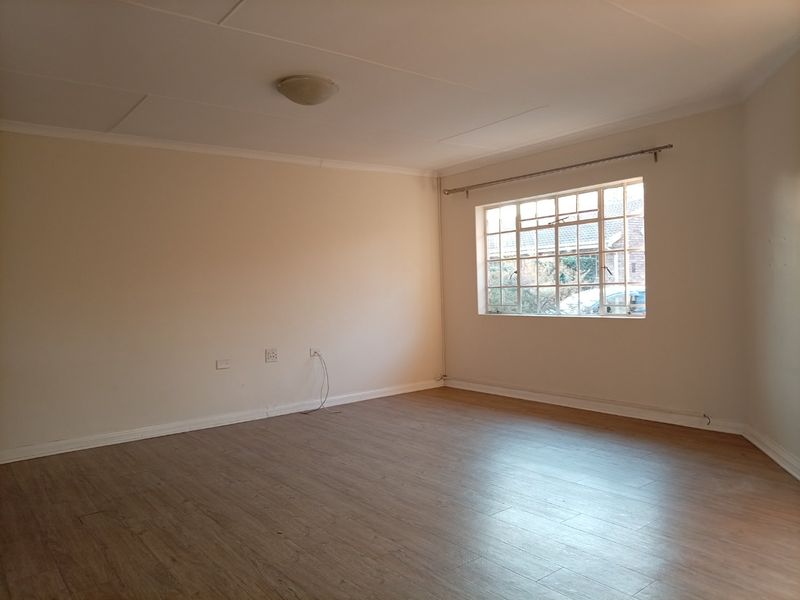 A bright, empty living room featuring neutral walls, laminate flooring, and a large steel-framed window, providing a blank canvas for interior design.