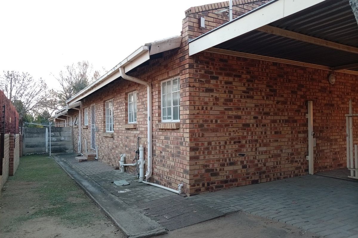 Rear view of the townhouse featuring a face brick facade, a covered carport, and a paved walkway leading along the side of the property.