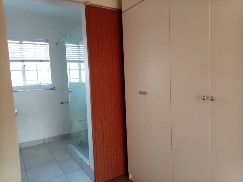 A bedroom featuring built-in cupboards and an adjoining en-suite bathroom with a glass shower enclosure and tiled flooring.