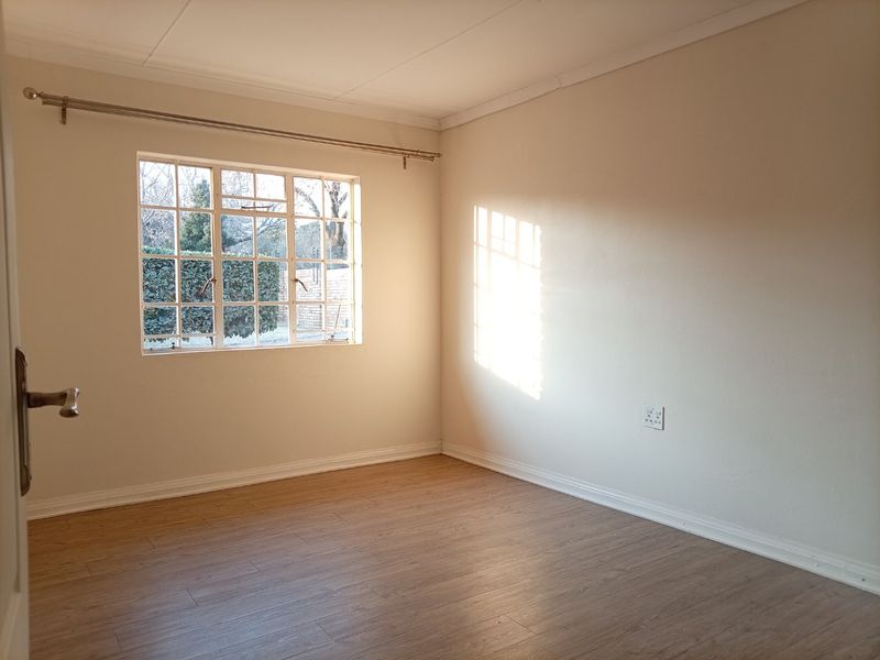 A bright, empty bedroom featuring laminate flooring, neutral walls, and a steel-framed window with a curtain rod.