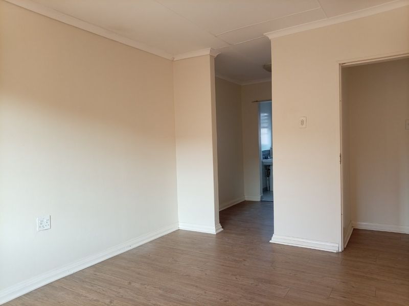 An empty living area featuring laminate flooring, neutral walls, and coved ceilings, with a clear view into an adjacent hallway and bathroom area.