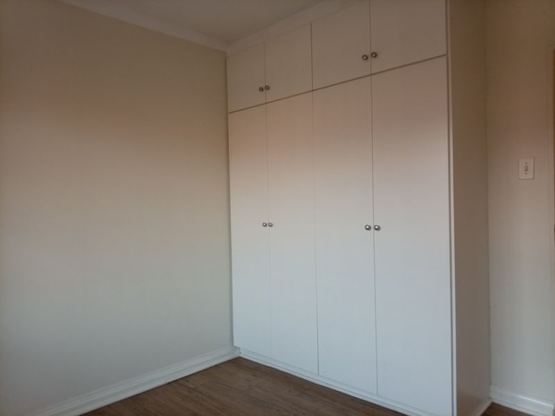 A clean, empty bedroom featuring neutral walls, laminate flooring, and ample built-in cupboard storage with overhead cabinets.