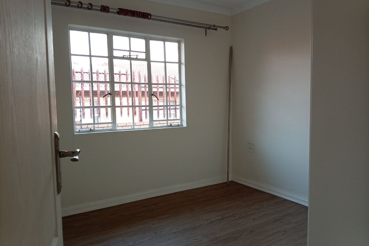 A clean, empty bedroom featuring laminate flooring, neutral walls, and a window with security bars, providing a blank canvas for personalization.