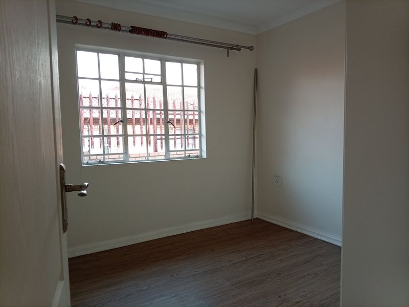 A clean, empty bedroom featuring laminate flooring, neutral walls, and a window with security bars, providing a blank canvas for personalization.