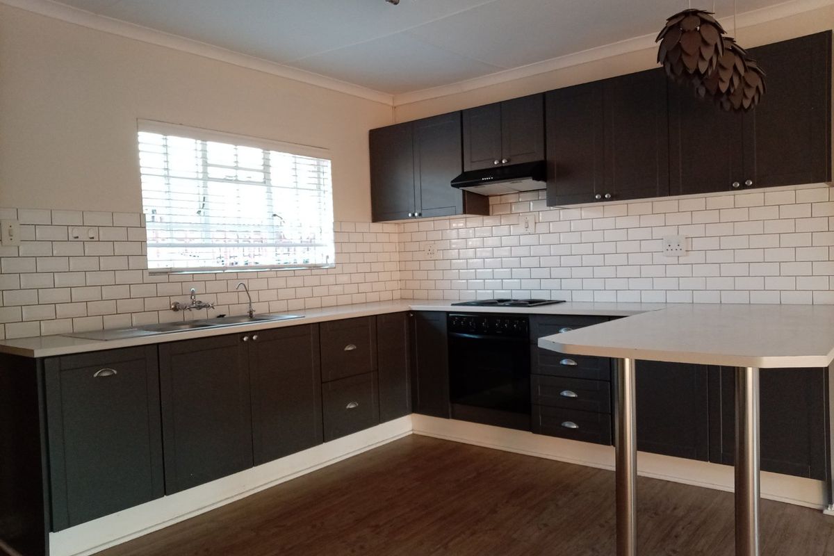 Modern kitchen featuring dark cabinetry, subway tile backsplash, built-in oven, hob, extractor fan, and a functional breakfast bar area.