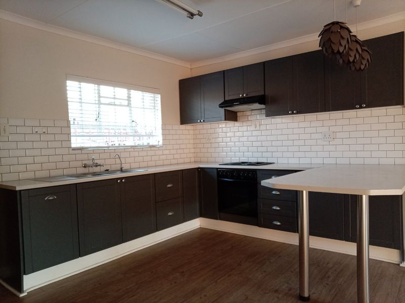 Modern kitchen featuring dark cabinetry, subway tile backsplash, built-in oven, hob, extractor fan, and a functional breakfast bar area.
