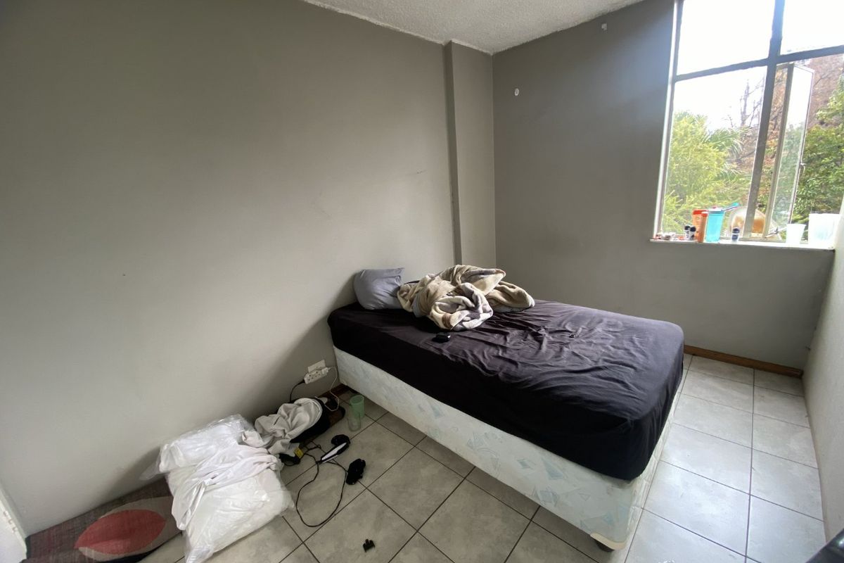 A bedroom featuring tiled flooring and a large window, providing natural light. The space requires cosmetic updates to the walls and ceiling.