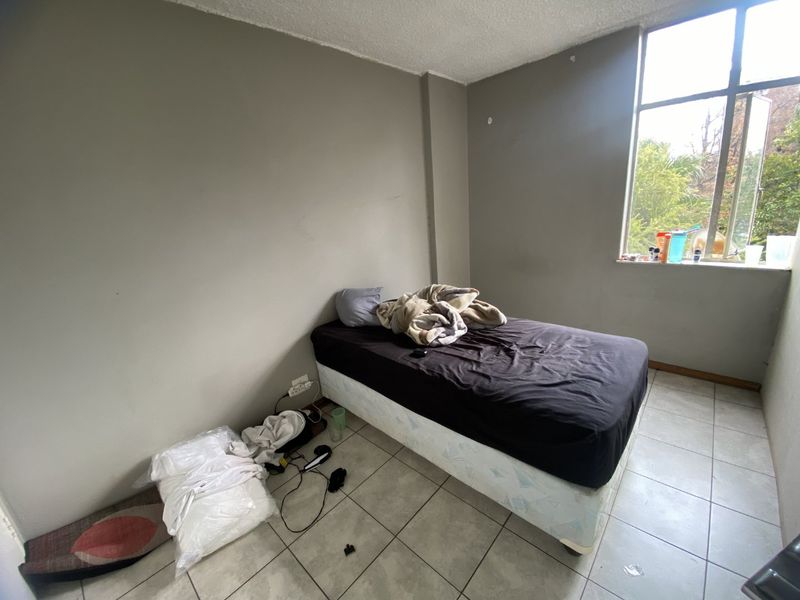 A bedroom featuring tiled flooring and a large window, providing natural light. The space requires cosmetic updates to the walls and ceiling.