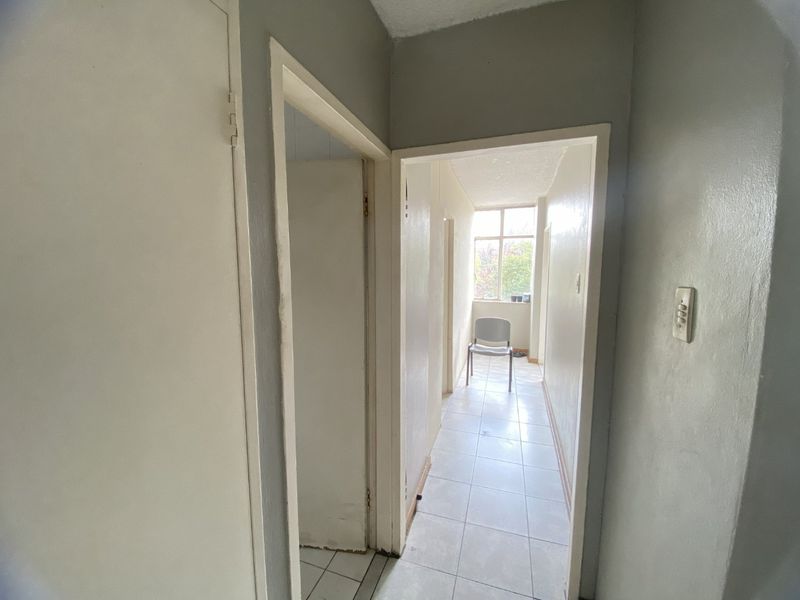 A functional hallway with tiled flooring and neutral wall paint, providing access to adjacent rooms and leading toward a naturally lit area.