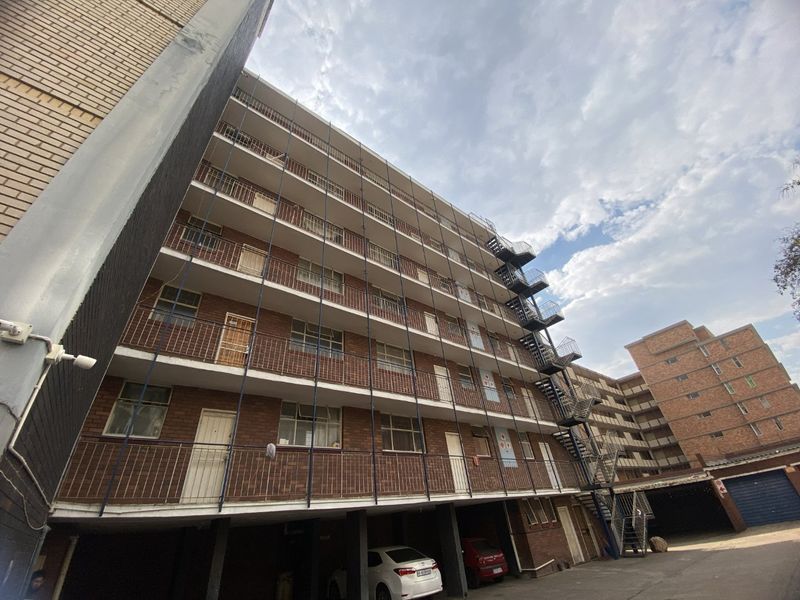 Exterior view of a multi-story apartment building featuring brick facade, external fire escape stairs, and ground-level covered parking.