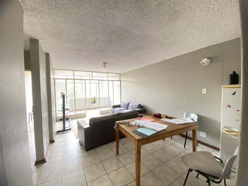 Open-plan living area featuring tiled flooring, a textured ceiling, and a glass-paneled partition leading to an enclosed balcony space.